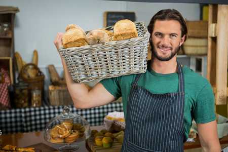 Portrait of male staff holding a basket of bread in bakery shopの写真素材