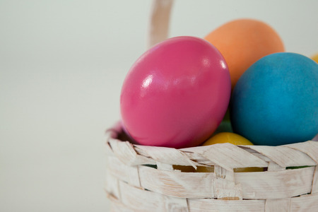 Various Easter eggs in wicker basket on white background