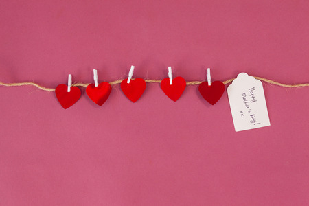 Happy mothers day card and red hearts hanging on rope against pink backgroundの写真素材