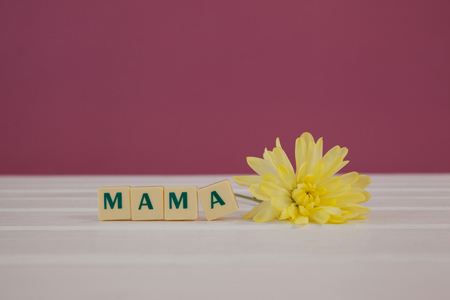 Yellow flowers next to blocks displaying mama message on wooden surfaceの写真素材