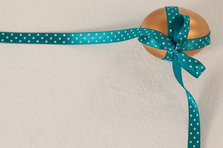 Golden easter egg tied with blue ribbon against white backgroundの写真素材