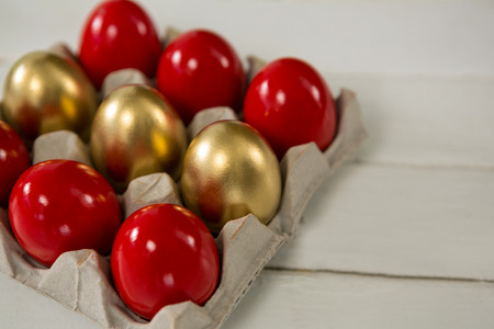 Close-up of red and golden Easter eggs in the carton on wooden background