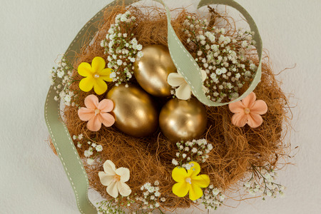 Golden easter eggs with flowers in nest against white background