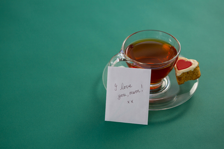 Tea with heart shape cookie and I love you mom text on card against green backgroundの写真素材