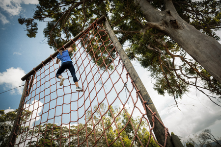 Woman climbing a net during obstacle course in boot campの写真素材