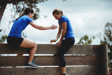 Female trainer assisting woman to climb a wooden wall during obstacle courseの写真素材