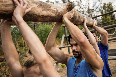 Fit people lifting a heavy wooden log during boot camp training