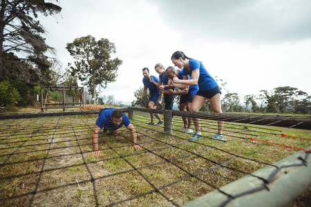 Fit man crawling under the net during obstacle course while fit people cheering in bootcampの写真素材
