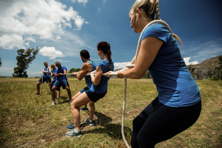 People playing tug of war during obstacle training course in boot camp