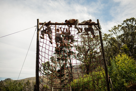 Military soldiers climbing rope during obstacle course in boot campの写真素材
