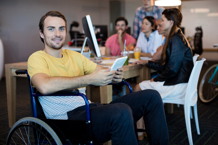 Portrait of physically disabled man on wheelchair using tablet in officeの写真素材