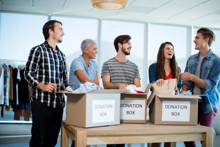 Happy creative business team sorting clothes in donation box in officeの写真素材