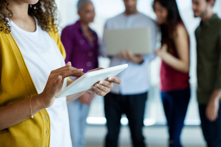 Mid section of woman using digital tablet in office while colleague discussing in background