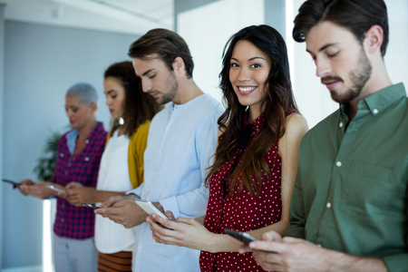 Portrait of smiling woman using mobile phone with their colleagues in officeの写真素材