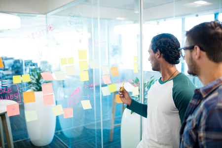 Creative business team looking at sticky notes and discussing in officeの写真素材