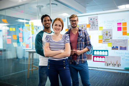 Portrait of smiling creative business team standing against sticky notes in office