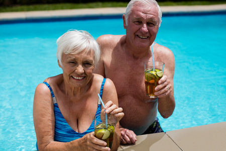Portrait of senior couple holding glasses of iced tea in poolの写真素材