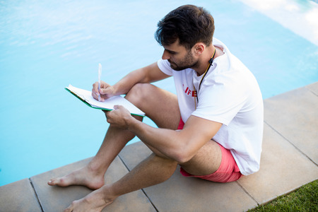 Lifeguard writing on clipboard at poolside on a sunny dayの写真素材