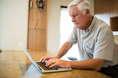 Senior man using laptop in the kitchen at homeの写真素材