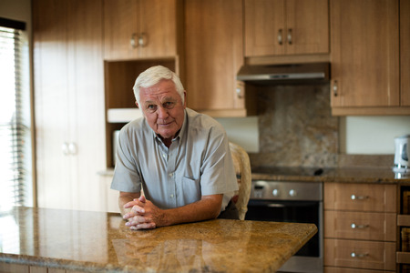Portrait of senior man sitting with hands clasped in the kitchen at homeの写真素材