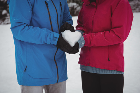 Mid section of couple in warm clothing holding snowy heart