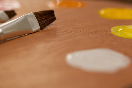 Wooden palette with multiple colors and paint brushes on wooden table