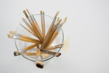 Close-up of various paintbrush in a glass jar on white background