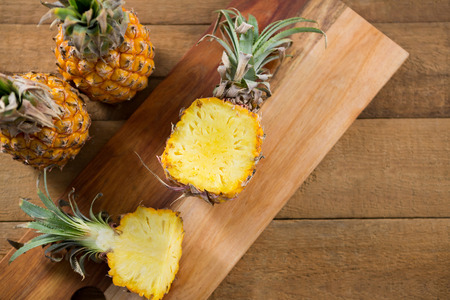 Overhead of halved pineapple on chopping board on wooden table