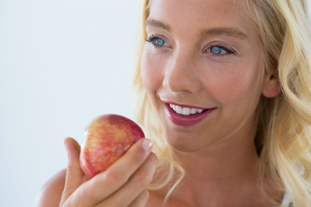 Close-up of beautiful woman holding red apple against white backgroundの写真素材