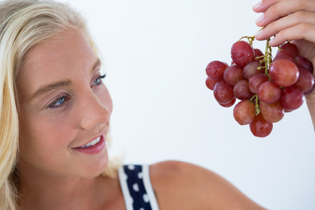 Beautiful woman looking at bunch of red grapes against white backgroundの写真素材