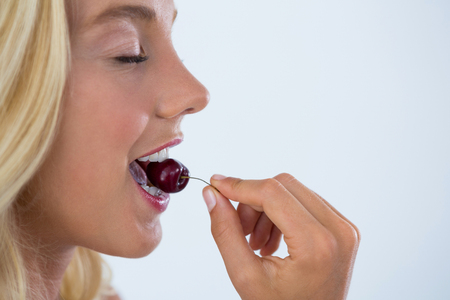 Clos-up of beautiful woman eating cherry against white backgroundの写真素材