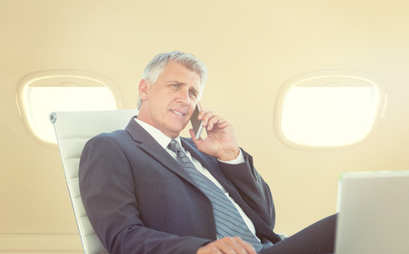 Businessman having a phone call  against sky seen through windowsの写真素材