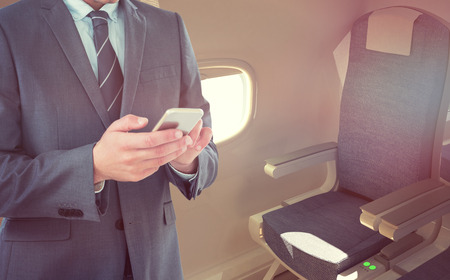 Smiling businessman using mobile phone against empty chairs in airplane