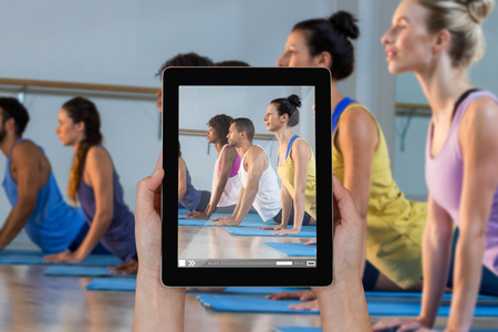 Close-up of hands holding digital tablet against group of people performing yogaの写真素材