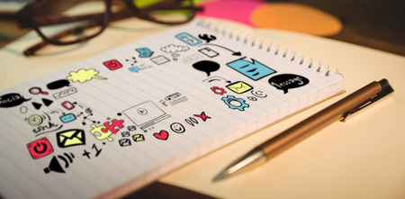 Composite image of various media icons against high angle view of notepad and pen on deskの写真素材