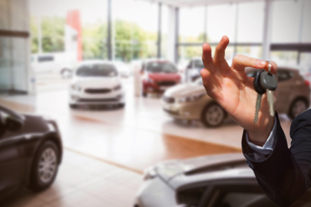 Happy seller holding car keys  against defocused image of cars parkedの写真素材
