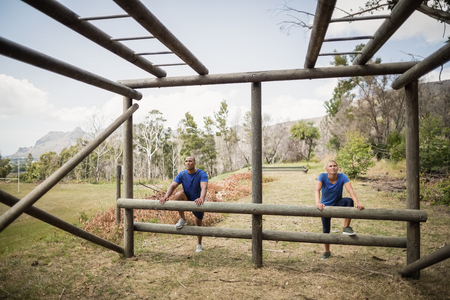 Fit man and woman climbing monkey bars during obstacle course in boot campの写真素材