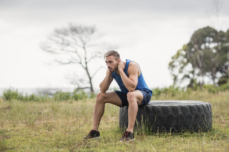 Tired fit man sitting on tire in boot campの写真素材