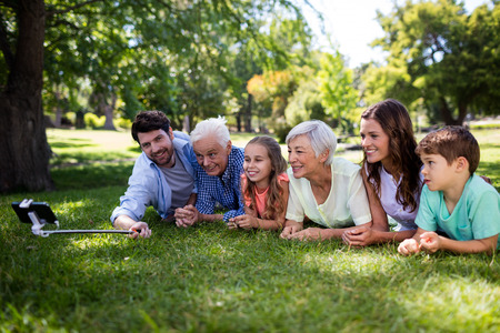 Multi generation family lying on grass and taking a selfie with selfie stickの写真素材