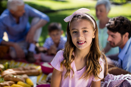 Portrait of girl with hairband and family enjoying the picnic in backgroundの写真素材