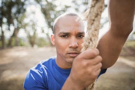 Portrait of fit man climbing rope during obstacle course in boot campの写真素材