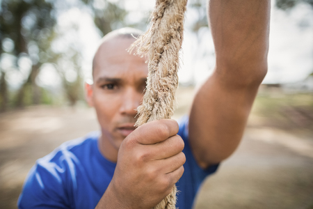 Portrait of fit man climbing rope during obstacle course in boot campの写真素材