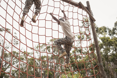 Military soldiers climbing a net during obstacle course in boot campの写真素材