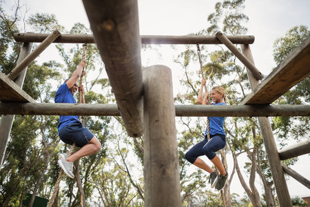 Fit man and woman climbing rope during obstacle course in boot campの写真素材