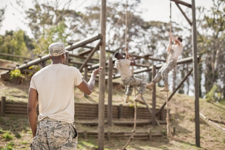 Military soldiers climbing rope during obstacle course training at boot camp
