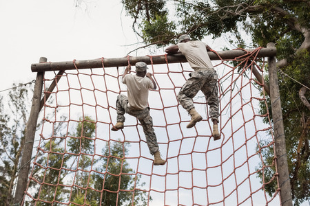 Military soldier climbing a net during obstacle course in boot campの写真素材
