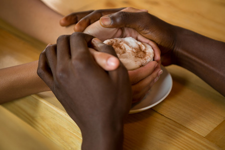 Close-up of couple holding hands and coffee cup in coffee shopの写真素材