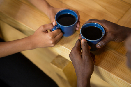 High angle view of couple hands holding coffee cups at table in cafeの写真素材
