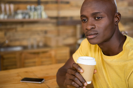 Thoughtful young man holding disposable coffee cup in cafeの写真素材