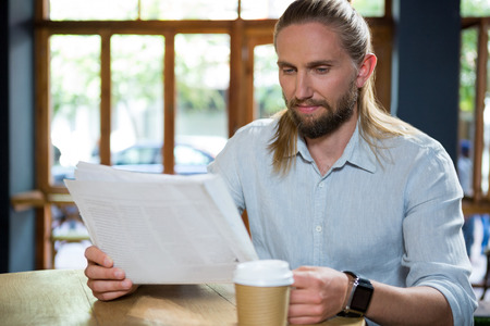 Handsome young man reading newspaper at table in coffee shopの写真素材